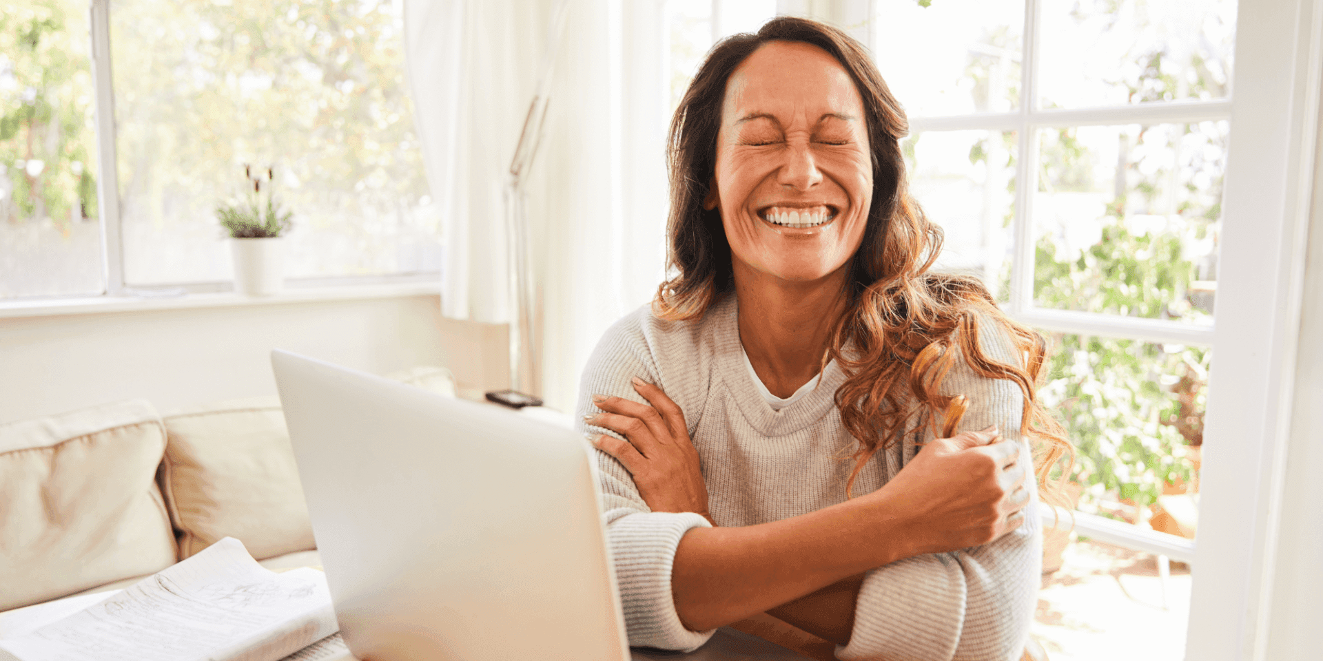 A woman sitting in front of her laptop, smiling with her eyes closed (demonstrating the use of humor in psychotherapy).